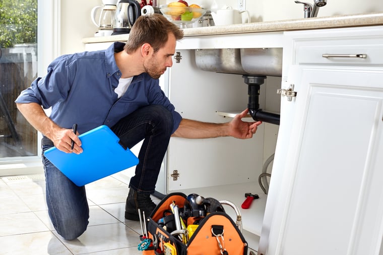 A plumber inspecting pipes under a kitchen sink.