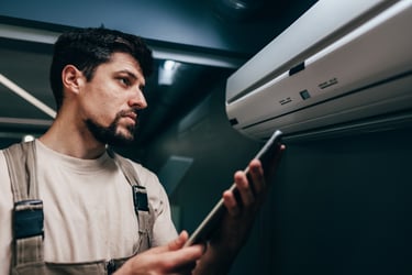 Technician inspects air conditioning unit while checking readings on a tablet in a modern indoor space