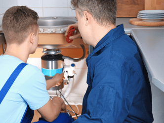 Plumber working with apprentice on a repair under a sink